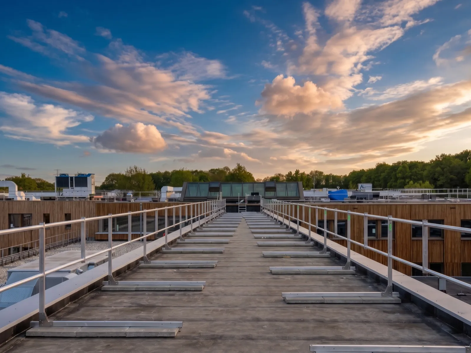 Flat roof at the IND site in Ter Apel with Protector Guardrail roof-edge protection along a walkway, with rooftop plant and an evening sky.