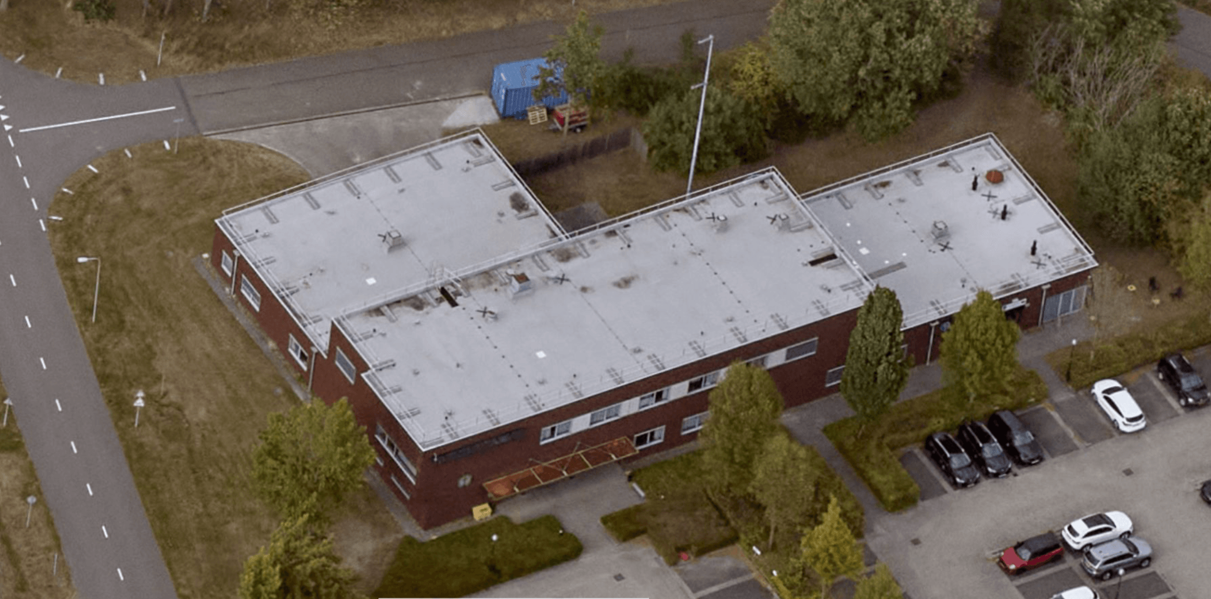 Aerial view of the L-shaped building at Vliegbasis Eindhoven with Protector Guardrail roof-edge protection along the flat roof perimeter.